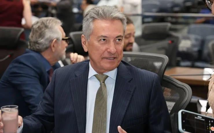 Roberto Hashioka fala durante sessão na Assembleia Legislativa de Mato Grosso do Sul, cercado por outros parlamentares e microfones da imprensa.
