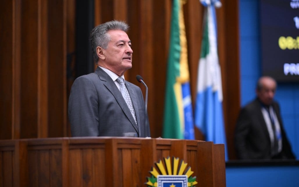 Roberto Hashioka discursa na tribuna da Assembleia Legislativa de Mato Grosso do Sul, com as bandeiras do Brasil e do Estado ao fundo.