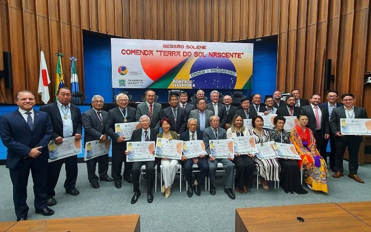 Homenageados e autoridades reunidos no plenário da Assembleia Legislativa, com os certificados nas mãos, sob o banner da sessão solene da Comenda Terra do Sol Nascente.