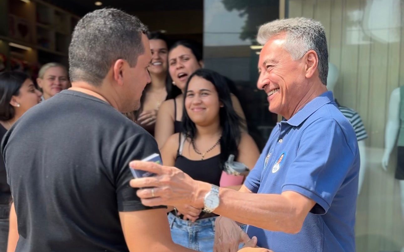 Roberto Hashioka cumprimenta um comerciante na porta de uma loja, cercado por trabalhadoras que acompanham a conversa.