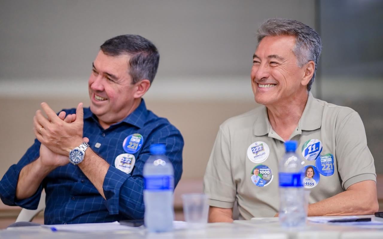 Roberto Hashioka, à direita, e Reinaldo Azambuja, sentados lado a lado à mesa, sorriem durante o encontro na Associação Esportiva e Cultural Nipo-Brasileira de Campo Grande.