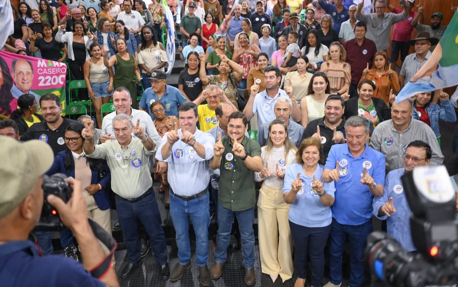 Roberto Hashioka e apoiadores fazem gesto de número um para a câmera durante evento em auditório lotado.